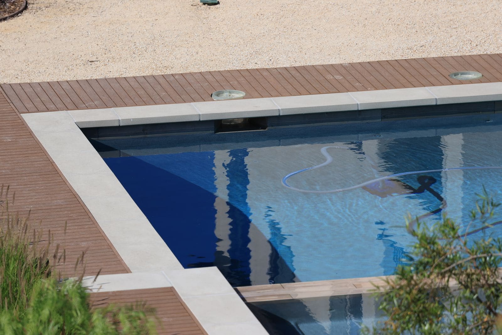 An automatic pool cleaner and its hose moving across a deck-edged pool